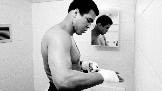 -Text:  Muhammad Ali tapes his hands in a restroom at Trinity High School, 4011 Shelbyville Road, before fighting a pair of exhibition matches at the school. Several amateur matches also were on the card for the Golden Gloves Benefit show last night. Dec. 10, 1976