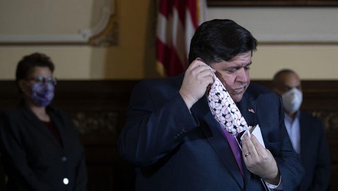 Gov. JB Pritzker puts on a mask during his daily coronavirus briefing at the Illinois Capitol on May 20, 2020, in Springfield.