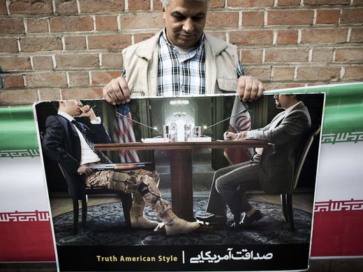 A man holds a poster that shows a U.S. negotiator holding a gun as he sits with an Iranian negotiator.