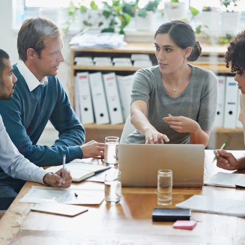 A group of co-workers discuss a project on a lapto