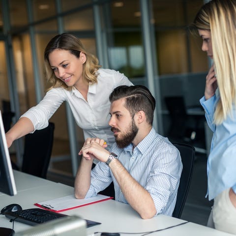 Three office workers gathered around a computer.