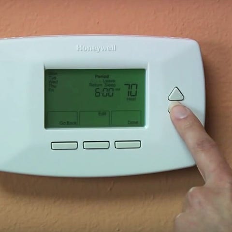 A person programs a thermostat for a furnace/HVAX 