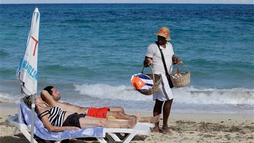 Tourists relax in the warm sun as a vendor sells kites decorated with Cuba's flag on a beach near Havana, Cuba, on Dec. 18, 2014.  A new set of U.S. government regulations takes effect Friday, Jan. 16, 2015, severely loosening the 50-decade long travel and trade restrictions for Cuba.
