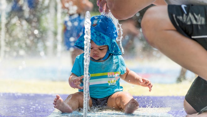 Paul Serrano of Visalia cools his daughter Natalia Serrano, 9 months, in the splash pad at Riverway Sports Park on Thursday, July 26, 2018.