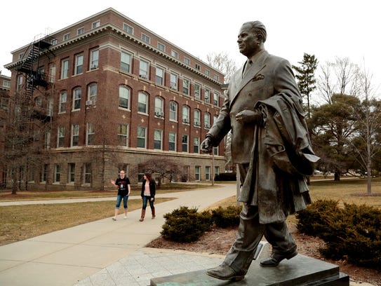 Students walk past the statue of John A. Hannah, MSU’s