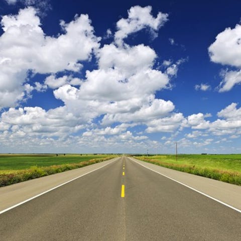 An open road and sky with puffy clouds