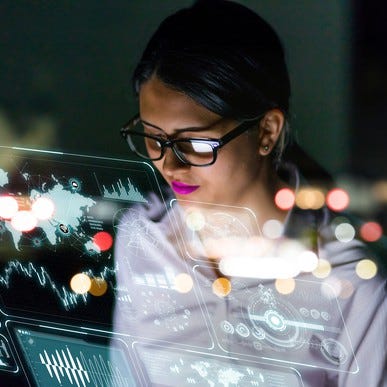Female engineer looking at data visualizations on multiple screens, reflected in glass.