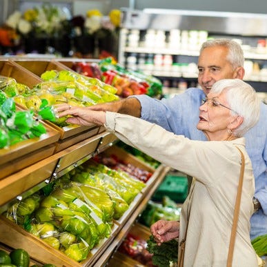 Senior couple at a supermarket, reaching for fruit in a bin.