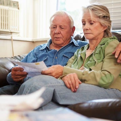 Senior man and woman on a couch looking at documents with concerned expressions.