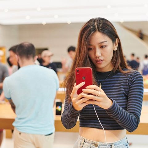 A woman looking at a red iPhone in an Apple store...