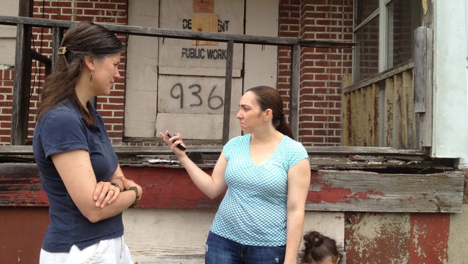 Camden Churches Organized for People worker Kristen Zielinski-Nalen speaks with Juana Placencia, whose daughter, Arisleida, stands next to her. Placencia hopes the city finally demolishes 936 N. 19th Street, an abandoned home without a roof that adjoins hers.