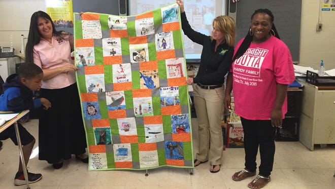 Kellyann Goring and Star Olson present a quilt featuring Olson's students' favorite books to Minnie Ruffin teacher Alicia Hardy.