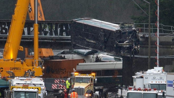 A damaged Amtrak train car is lowered from an overpass at the scene of Monday's deadly train crash onto Interstate 5 on Tuesday. Federal investigators say they don't yet know why the Amtrak train was traveling 50 mph over the speed limit when it derailed Monday south of Seattle.
