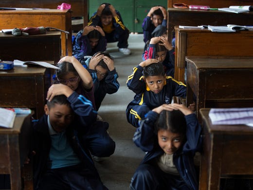 Nepalese school children crouch under their desk during