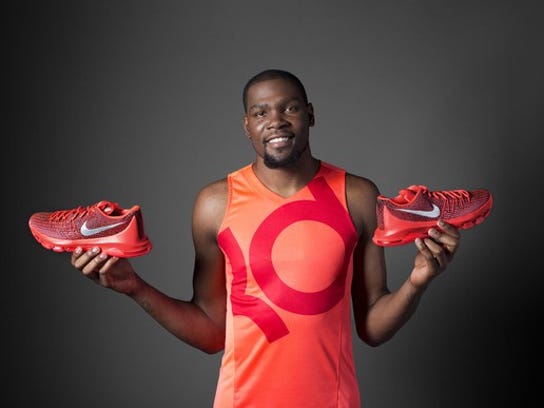 NBA star Kevin Durant holding a pair of his signature Nike shoes in red and orange.