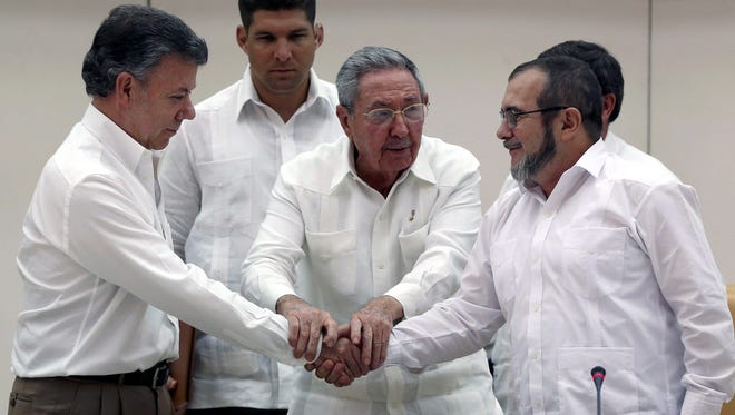 Cuban President Raul Castro holds the hands of Colombian President Juan Manuel Santos, left, and top leader of the Revolutionary Armed Forces of Colombia (FARC) Rodrigo Londono 'Timochenko' Echeverri during a press conference announcing an agreement between the two parts after nearly three years of peace negotiations, in Havana, Cuba, Sept. 23, 2015.