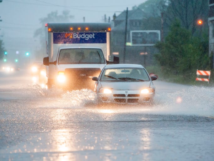 Cars drive through flooded roadways.