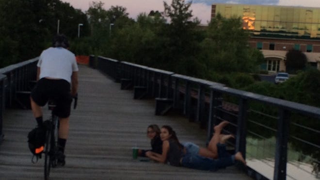 Tom Mueller cycles past a couple of teens enjoying the evening on the bike/ped bridge in downtown Wausau.