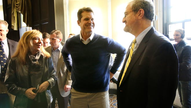 Michigan football coach Jim Harbaugh, center, talks with U-M President Mark Schlissel, right, after a news conference in Ann Arbor on Friday, Jan. 29, 2016.
