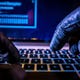 A gloved hacker typing on a keyboard in a dark room.