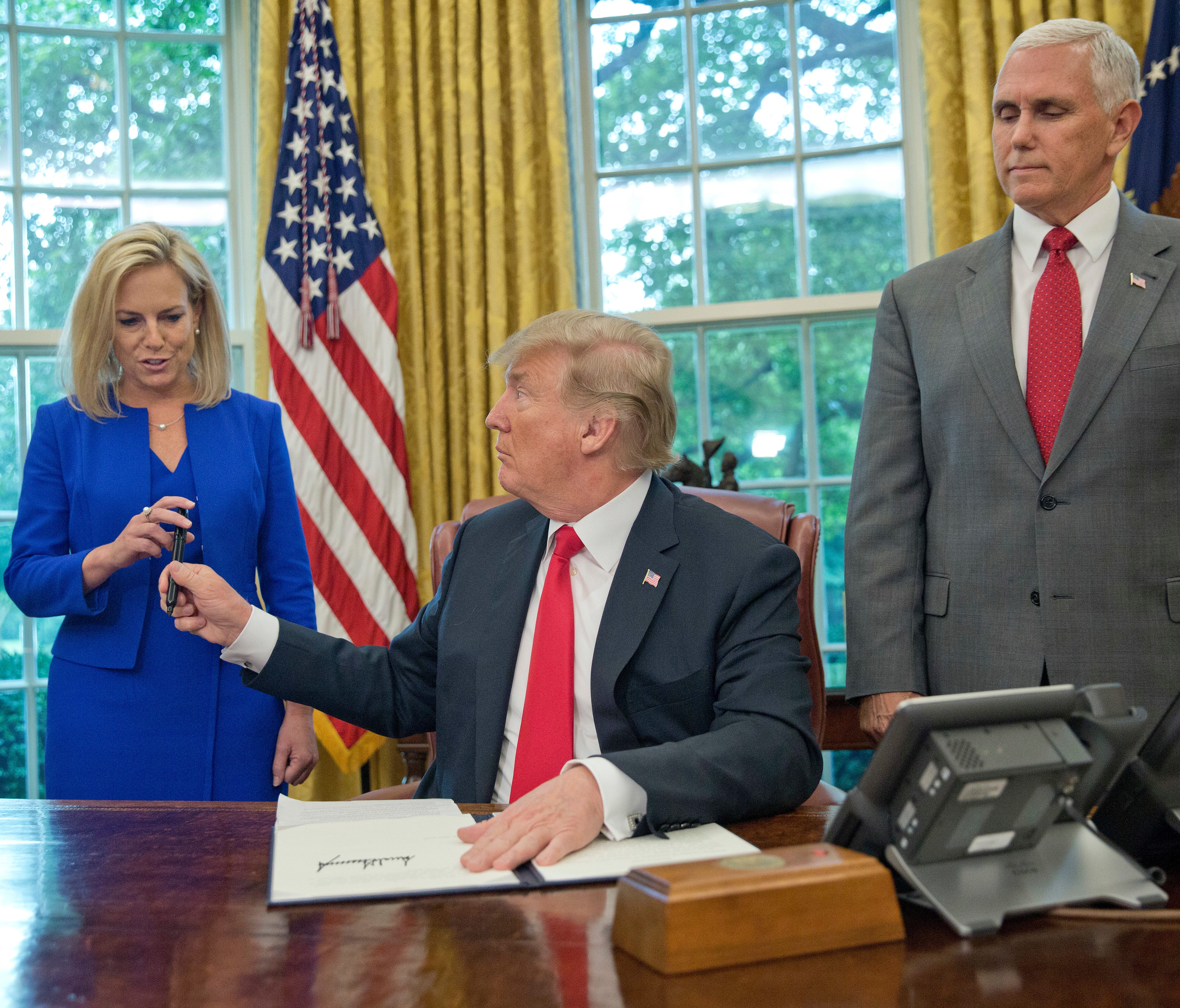 President Donald Trump gives the pen he used to sign the executive order to end family separations to Homeland Security Secretary Kirstjen Nielsen.