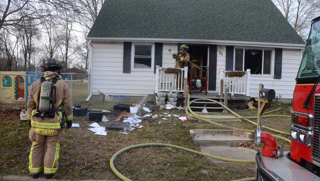 Firefighters spray some of the materials removed from the house at 24 Mosher Ave. after a fire started in the living room.