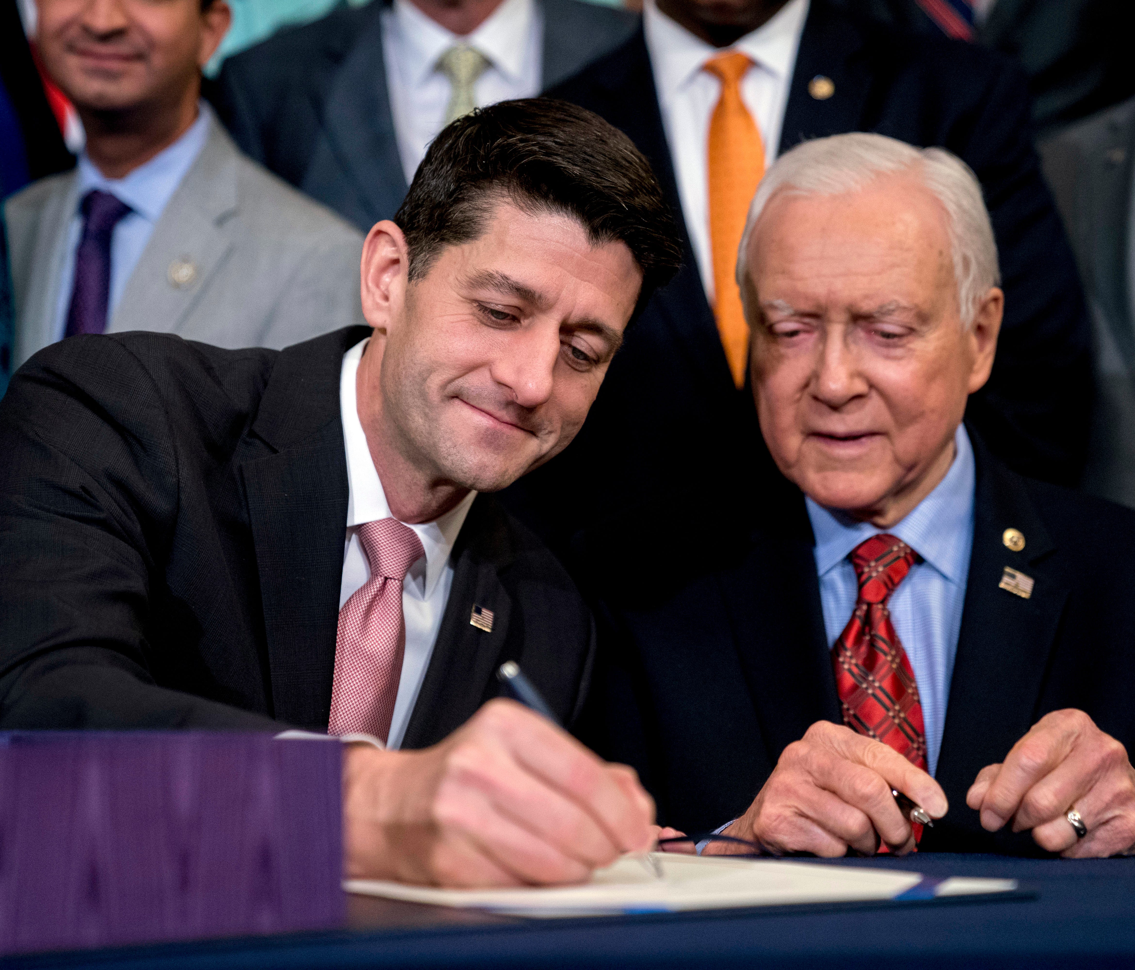 Speaker of the House Paul Ryan, R-Wis., center, accompanied by Senate Finance Committee Chairman Orrin Hatch, R-Utah, right, signs the final version of the GOP tax bill during an enrollment ceremony at the Capitol in Washington, Thursday, Dec. 21, 20