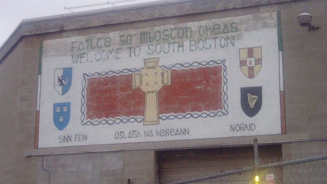 A mural in South Boston says "Welcome to South Boston" in English and "Faitre go mBoston dheas" in Irish. Also shown is a Celtic cross, the coats of arms of the Provinces of Ireland and the words "Sinn Fein," "Irish Republican Army" and NORAID." This mural has been torn down along with the building to make way for resident housing. Photo from/wikipedia.org