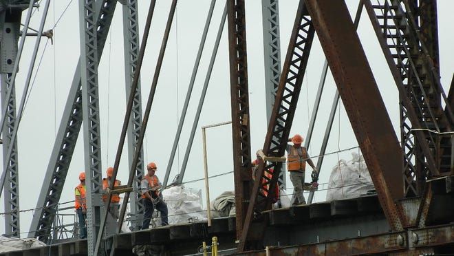 
Workers on the bridge Friday between the section that has been freshly painted and the rusty trusses that have not been worked on yet.
