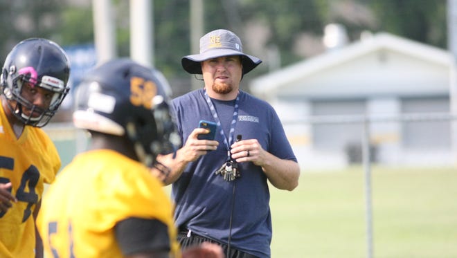 Northeast coach Chad Watson holds up his cell phone as he records his team during linemen drills Wednesday morning at Northeast High School.
