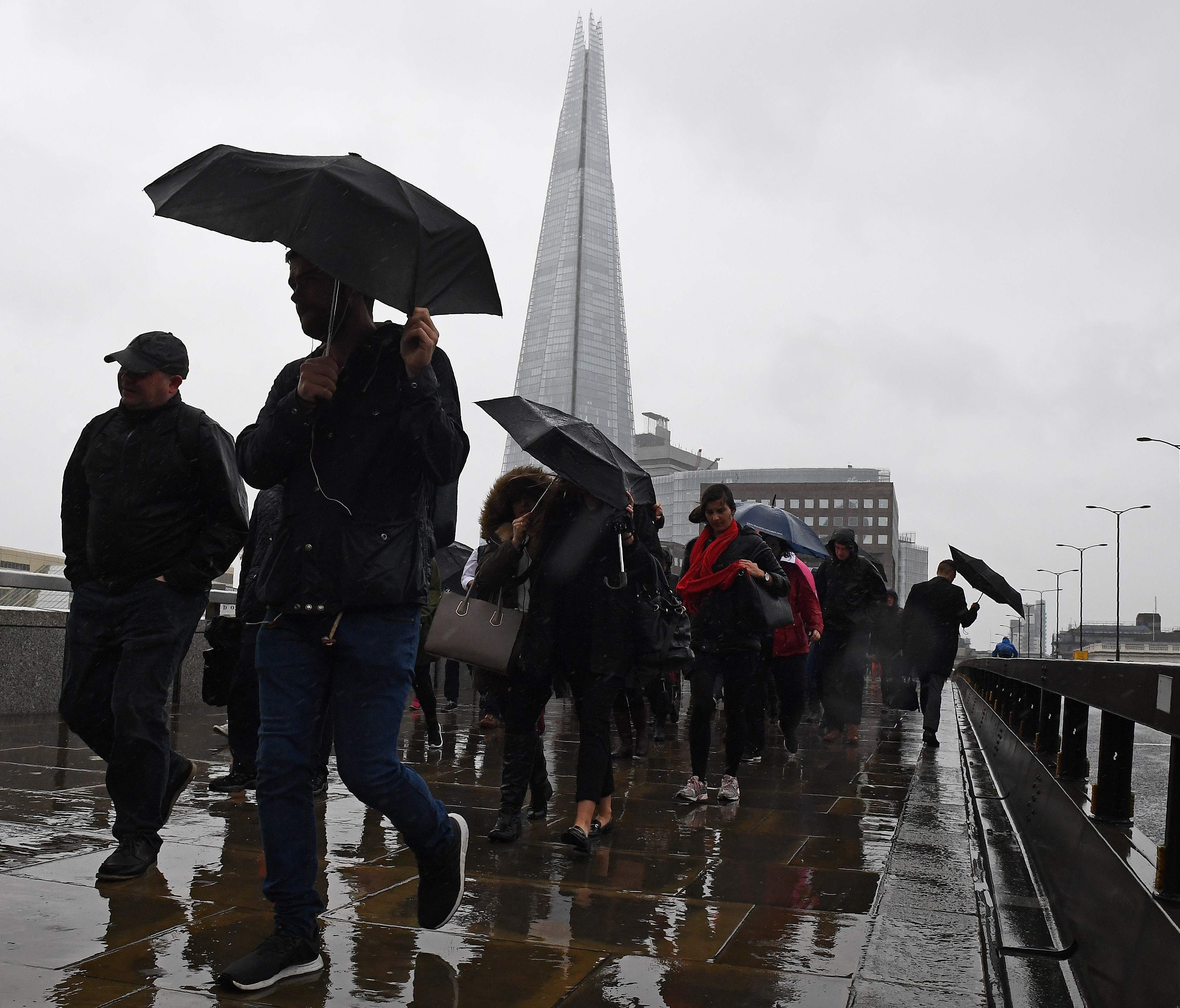 Commuters walk in the rain past a security barrier installed between the pavement and the road on London Bridge in London on June 6, 2017, as the police investigations continue following the June 3 terror attack.