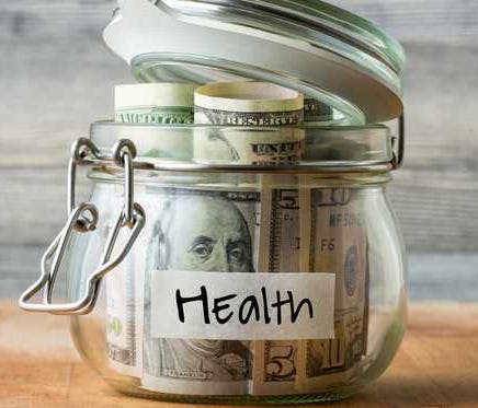 A glass money jar labeled health that's full of cash.