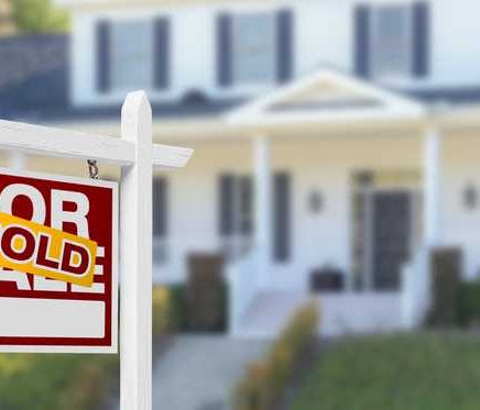 A home in the background with for sale/sold sign in foreground.