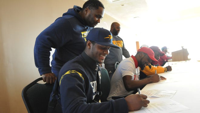 East English Village football head coach Rod Oden, standing far left, watches as his players, Desjuan Johnson, left, and Zhamaine March, middle, sign letters of intent to play football in college. Seated at right is Jaeveyon Morton of Detroit King. who is also signing.
