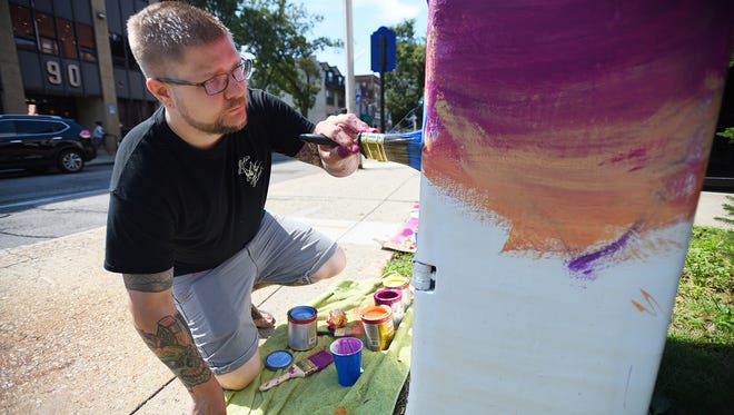 Johnny Newcomb of Bergenfield, an artist and tattooist, paints a utility box at the corner of Main and Atlantic streets in Hackensack on Wednesday.
