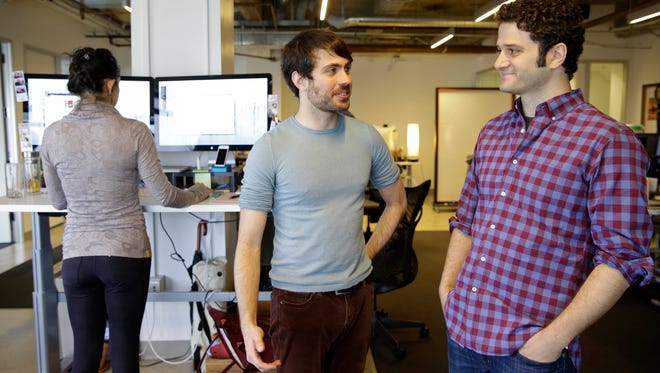 In this photo taken Thursday, April 3, 2014, Asana co-founders Justin Rosenstein, center, and Dustin Moskovitz, right, pose for photos at the company's headquarters in San Francisco. Asana peddles software that combines the elements of a communal notebook, social network, instant messaging application and online calendar to enable teams of employees to share information and do most of their jobs without relying on email. (AP Photo/Eric Risberg)