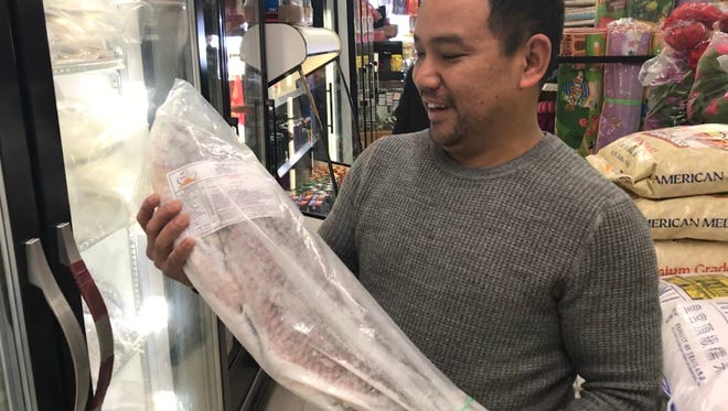 Store owner Durga Gurung holds up a frozen rohu fish at Dragon Asian Market Tuesday, Feb. 20, 2018.