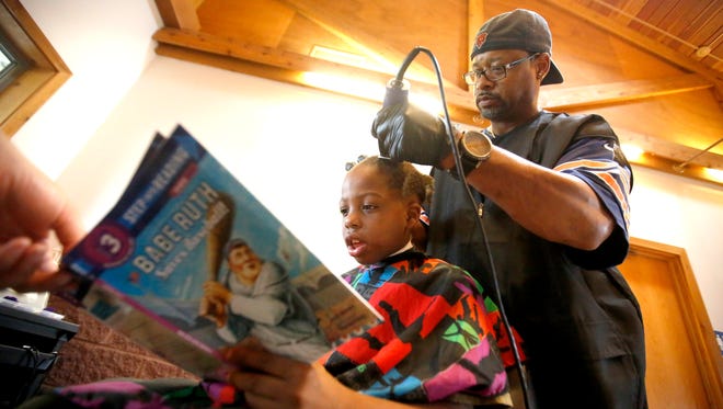 Courtney Holmes, right, listens to Jeremiah Reddick, 9, of Dubuque, as he reads while receiving a free haircut during the Back to School Bash on Saturday, Aug. 8, 2015 in Comiskey Park, in Dubuque, Iowa. Holmes offered his services to children who read while getting their hair cut.