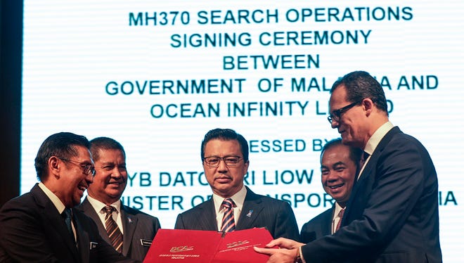 Malaysia Transport Minister Liow Tiong Lai, center, looks at the exchange of documents between Director General Civil Aviation Malaysia Azharuddin Abdul Rahman, left, and CEO Ocean Infinity Limited Oliver Plunkett, right, during a signing ceremony between the Malaysian government and Ocean Infinity Limited at the Transport Ministry building, in Putrajaya, Malaysia, Jan. 10, 2018.