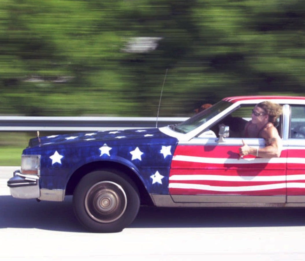 It's a holiday weekend, so let's look at some of the most patriotic cars out there. Here, Chris Maley gives the thumbs up to other drivers as he acknowledges their honks while he drives his flag painted 1985 Cadillac