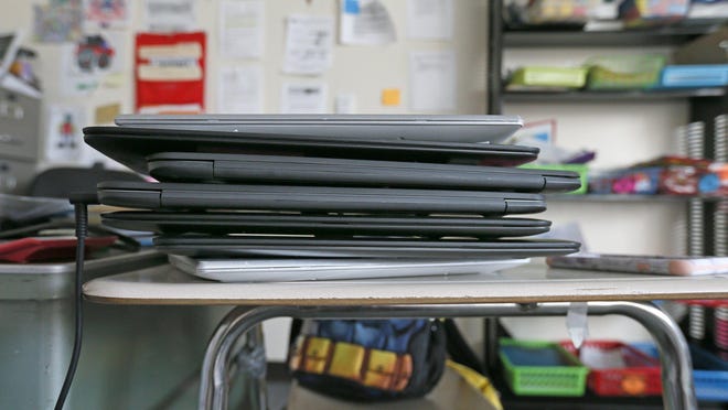 A stack of laptops sits in a classroom.