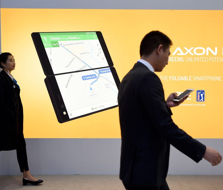 Two people walk past a billboard announcing the new ZTE's dual screens foldable smartphone AXON M on the first day of the Mobile World Congress (MWC) on February 26, 2018 in Barcelona.