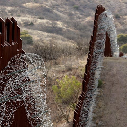 A razor-wire-covered border wall separates the...