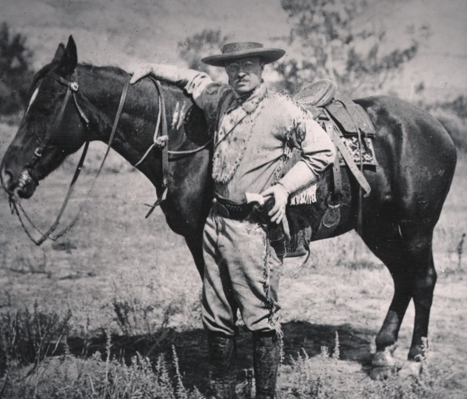 President Theodore Roosevelt stands with a saddled horse in the Badlands of western North Dakota.