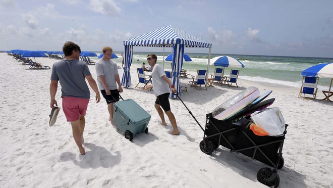 Harrison Neville, right, and Michael Bayeux, center, with Cabana Man beach service, help Seaside visitor Joseph Simpson, left, carry beach gear for he and his family Friday morning, on the first day of the reopening of Seaside's commercial district. To ensure social distancing, Seaside is prohibiting personal chairs, umbrellas and tents on the beach. The beach service company Cabana Man will be managing Seaside's beach, providing chair sets and umbrellas and offering food and beverage service from Seaside restaurants.