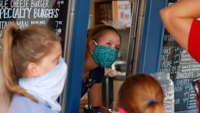 FILE - In this Aug. 4, 2020 file photo, a staffer wears a mask while taking orders at a small restaurant in Grand Lake, Colo., amid the coronavirus pandemic.  The coronavirus pandemic has put millions of Americans out of work. But many of those still working are fearful, distressed and stretched thin, according to a new poll by The Associated Press-NORC Center for Public Affairs Research.