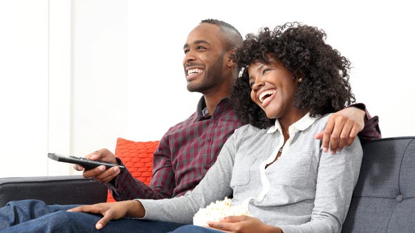 Two people watch TV snuggled up on the couch.