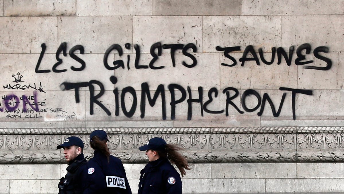 Police officers pass by a graffiti sprayed on the side of the Arc de Triomphe which reads 'the yellow vests will triumph' on Sundaym a day earlier after riots next to the Champs Elysee in Paris.