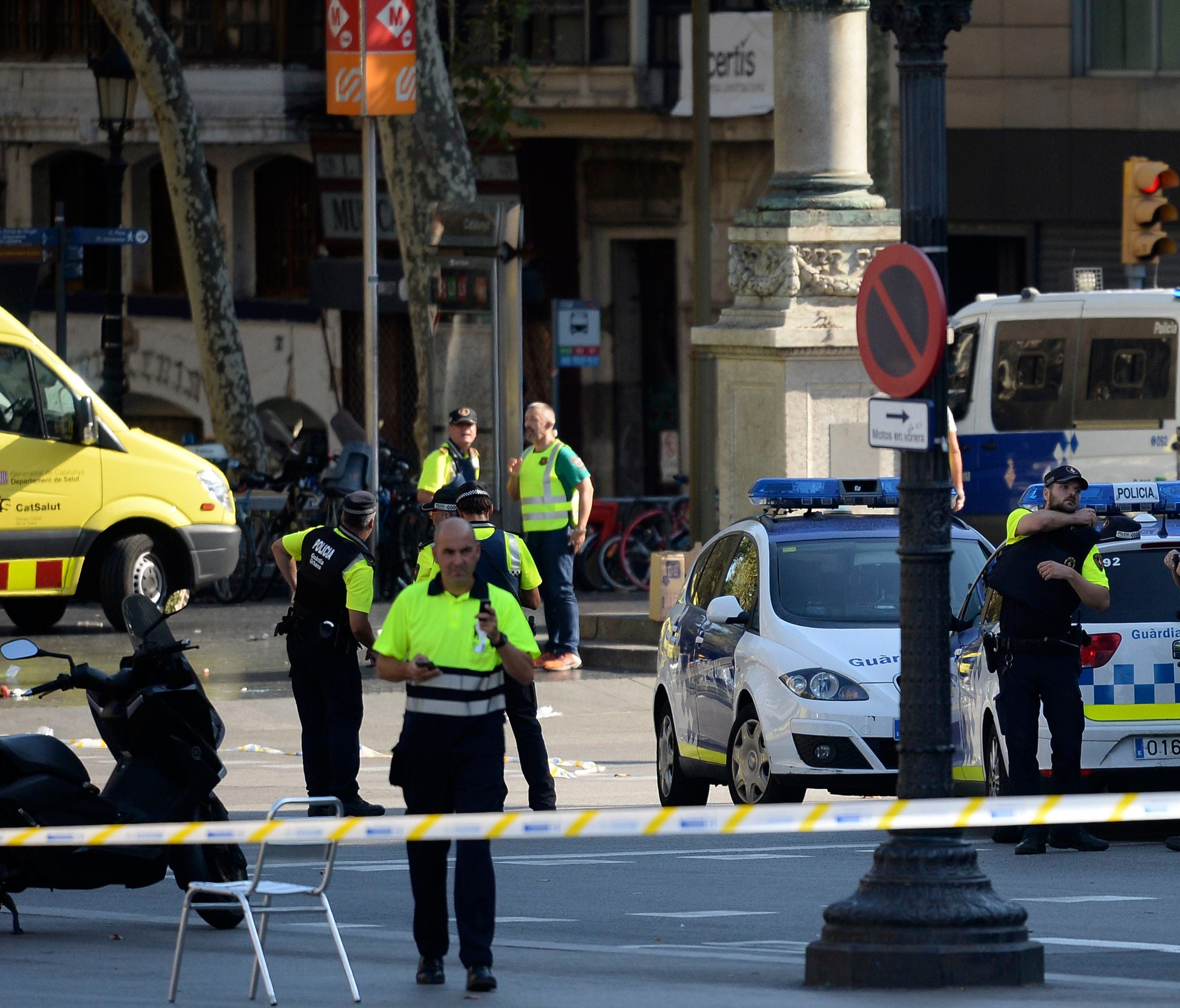 Medical staff members and policemen stand in a cordoned off area after a van plowed into the crowd, injuring several persons on the Rambles in Barcelona.