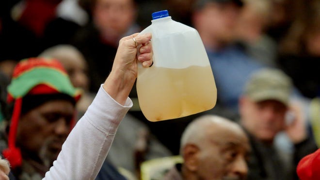 Flint resident Gladyes Williamson-Bunnell holds a sample of water that came from her home she saved from August 2014 after Flint switched from getting it's water from Detroit to using the Flint River water as a drinking source while officials spoke to a crowd about the water quality issues at a town hall meeting in the Flint City Hall dome in January 2015.